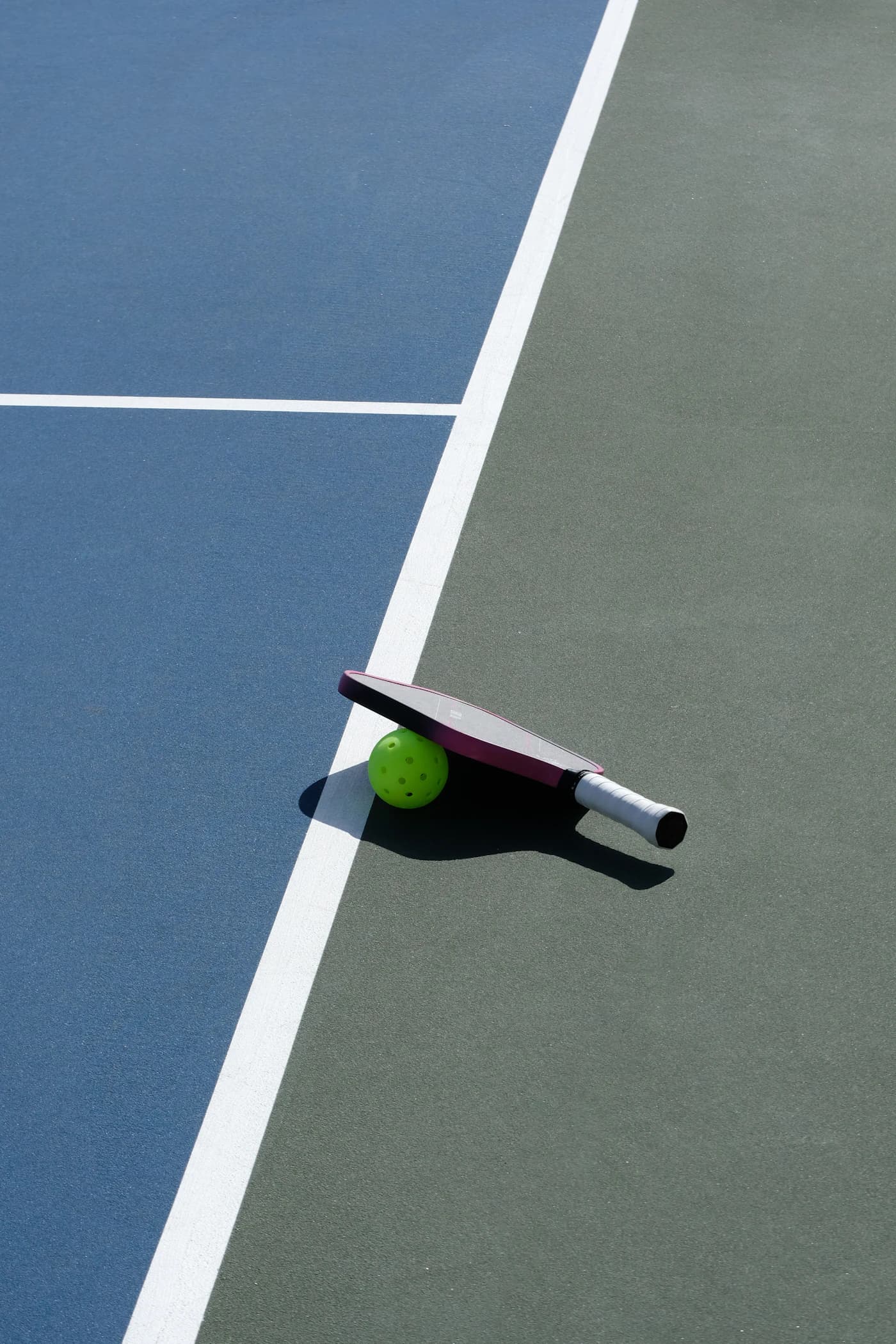 Pickleball paddle and bright green ball beside white court lines